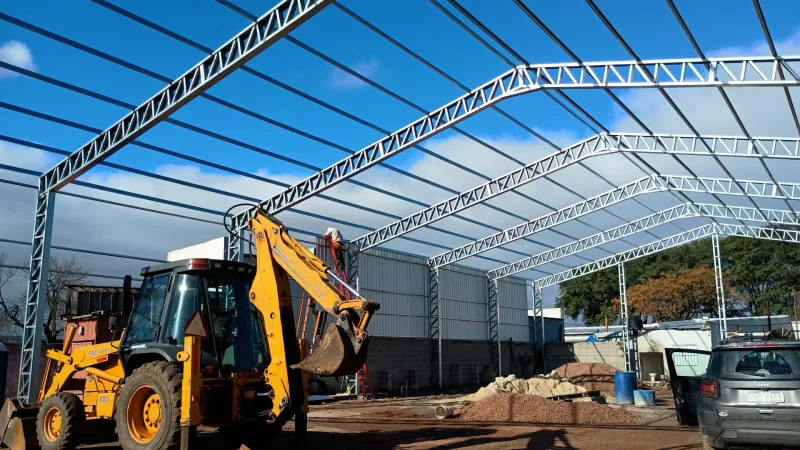 Estructura galvanizada en montaje con retroexcavadora trabajando en el terreno