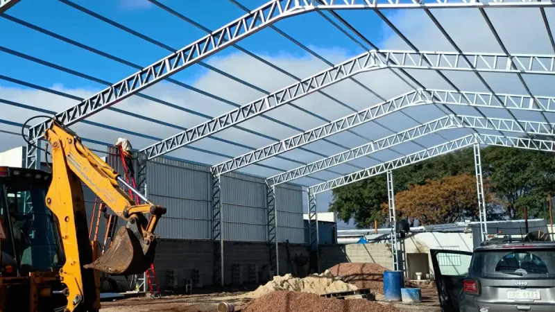 Otro ángulo: estructura galvanizada en montaje con retroexcavadora trabajando en el terreno
