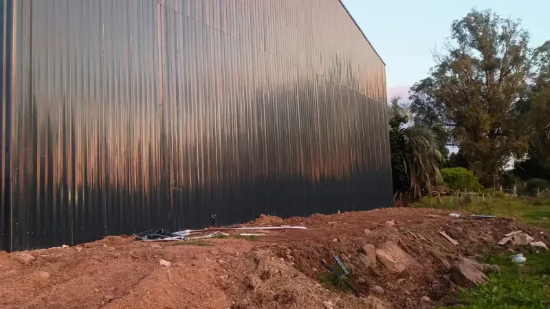 Otro ángulo: galpón cerrado de chapa de color oscuro con techo a dos aguas en terreno rural