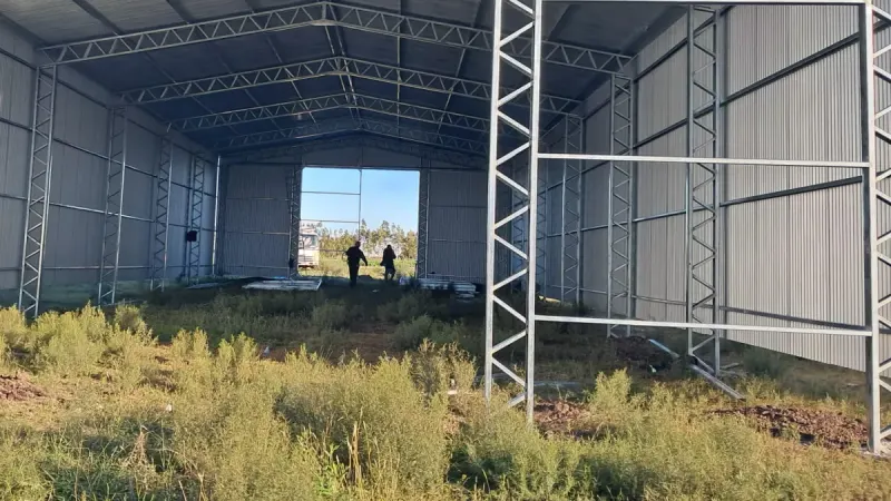 Otro ángulo: interior de un galpón galvanizado cerrado visto desde el portón, con cerchas a la vista