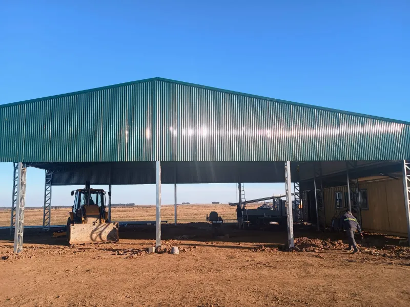 Tinglado abierto de chapa verde con una retroexcavadora debajo en campo abierto