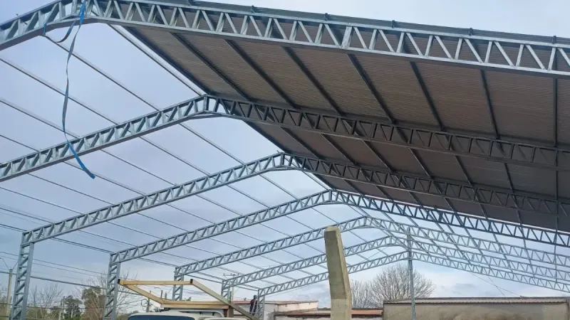 Vista parcial: tinglado galvanizado en predio urbano con el camión de montaje estacionado debajo