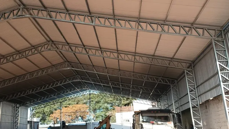 Otro ángulo: tinglado galvanizado abierto con un camión y dos camionetas bajo la cubierta